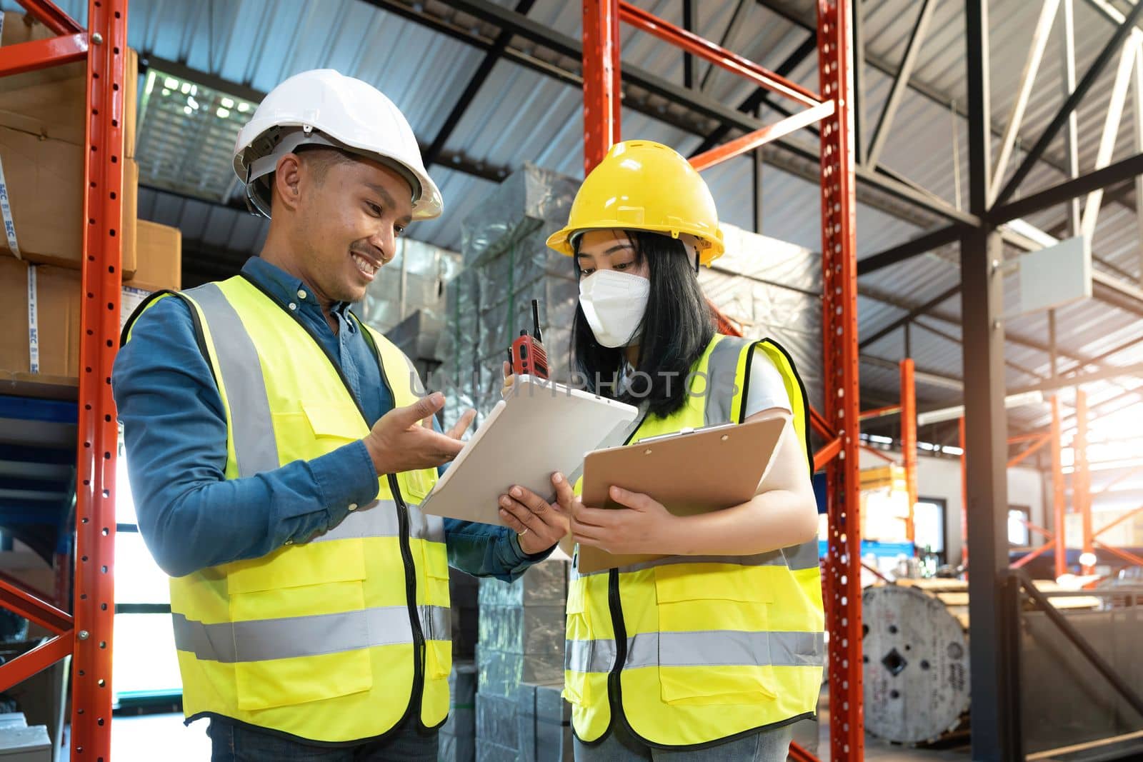 Professional adult Asian male warehouse manager and female worker are working together, checking their inventory in the warehouse or storehouse. by wichayada