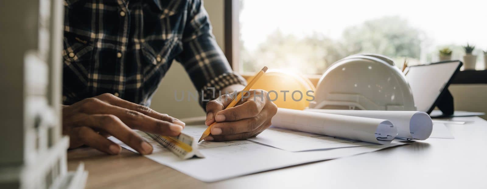 Image of engineer drawing a blue print design building or house, An engineer workplace with blueprints, pencil, protractor and safety helmet, Industry concept by wichayada