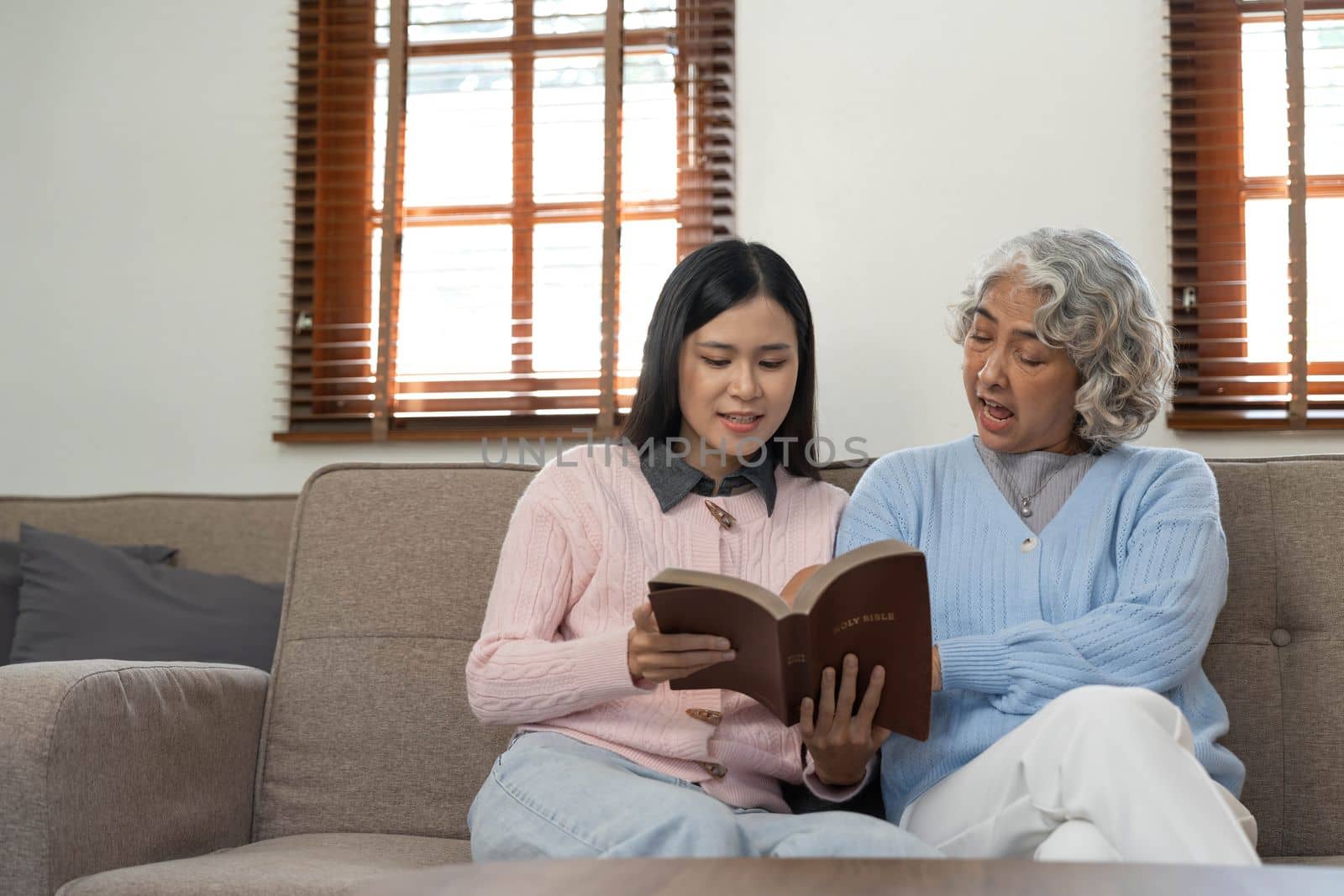Woman reading a book while sitting with happy grandmother at home.