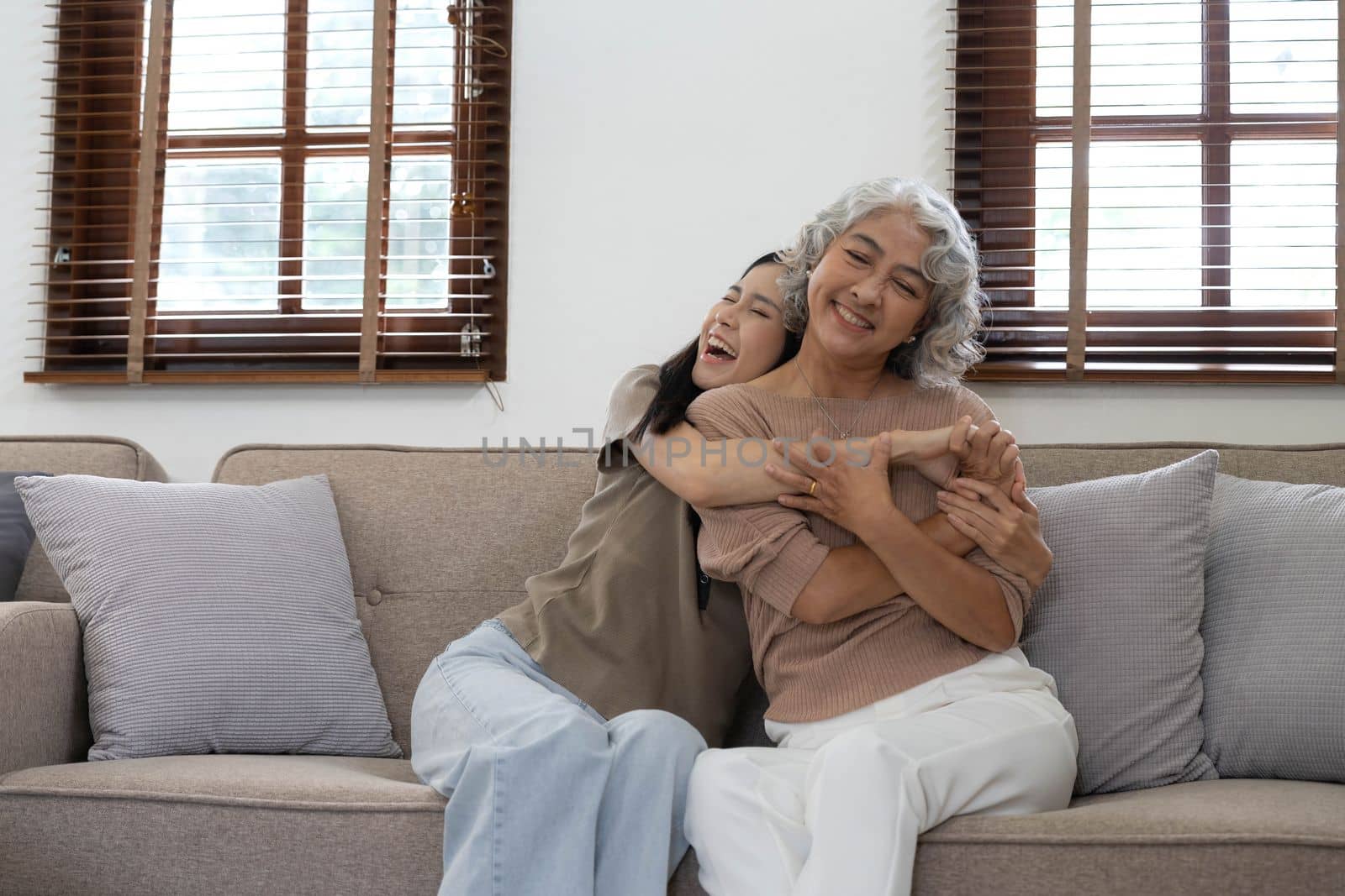 Portrait of Asian lovely family, young daughter hugging older mother. Attractive woman and senior elder mature mom sit on sofa, enjoy activity at home together in living room