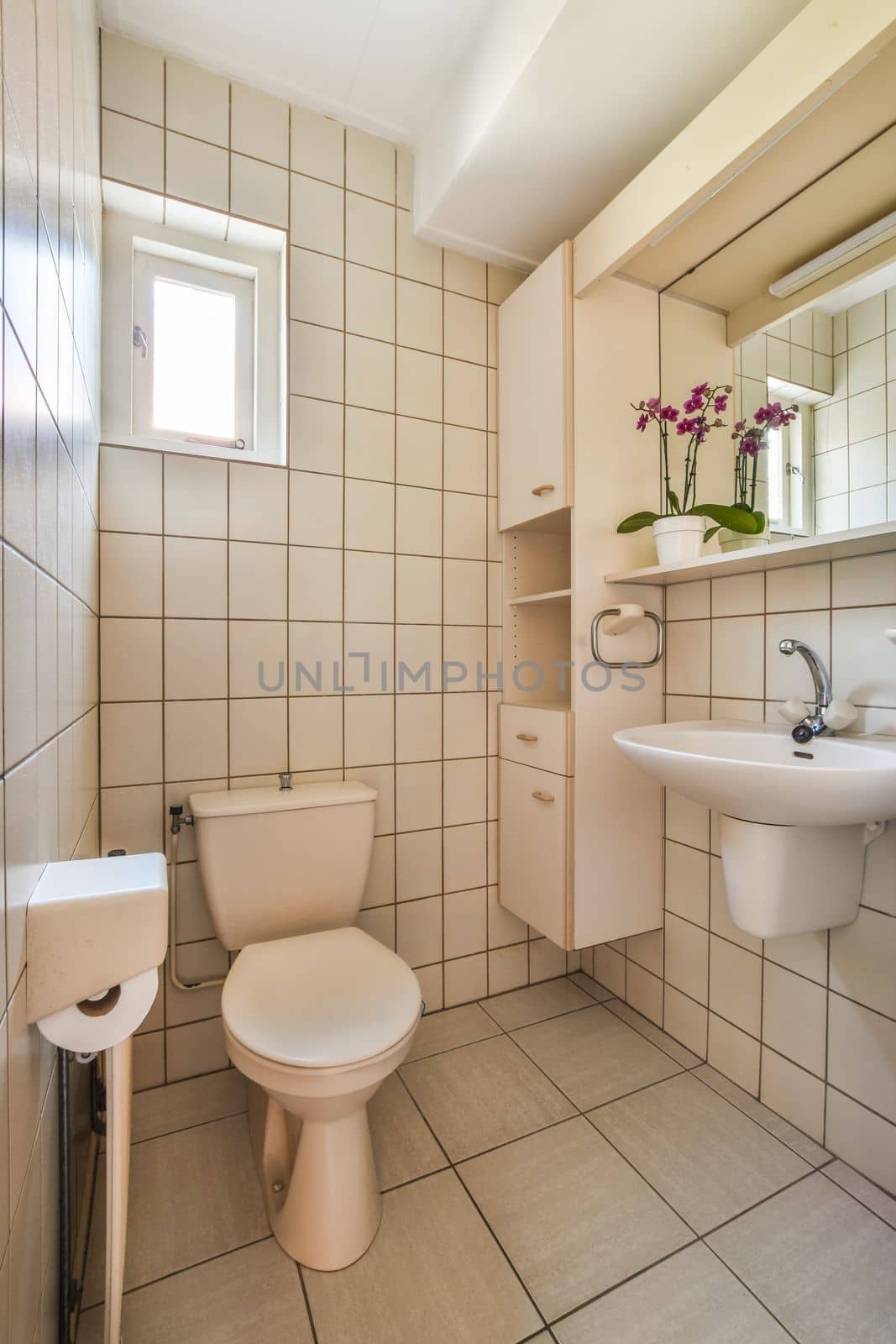 Wall hung toilet and small sink in corner in lavatory room with beige tile