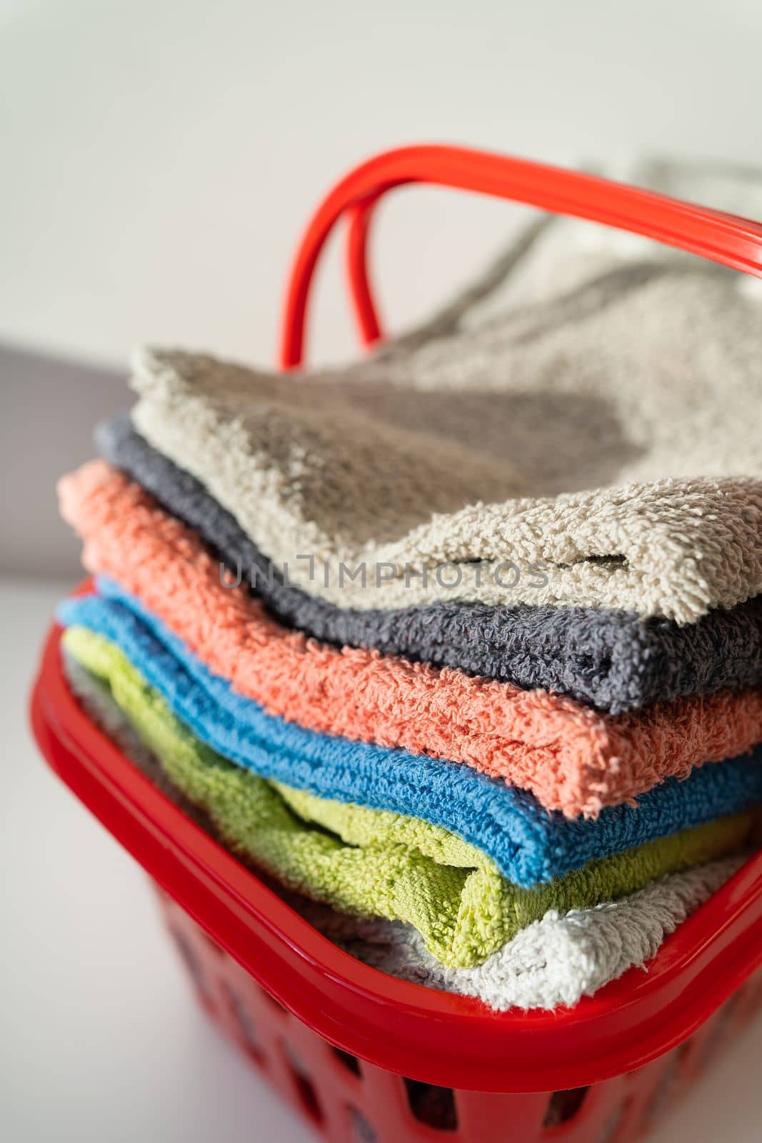 Multi-colored towels lie in a red laundry basket on a white background. Washing and ironing clothes, top view