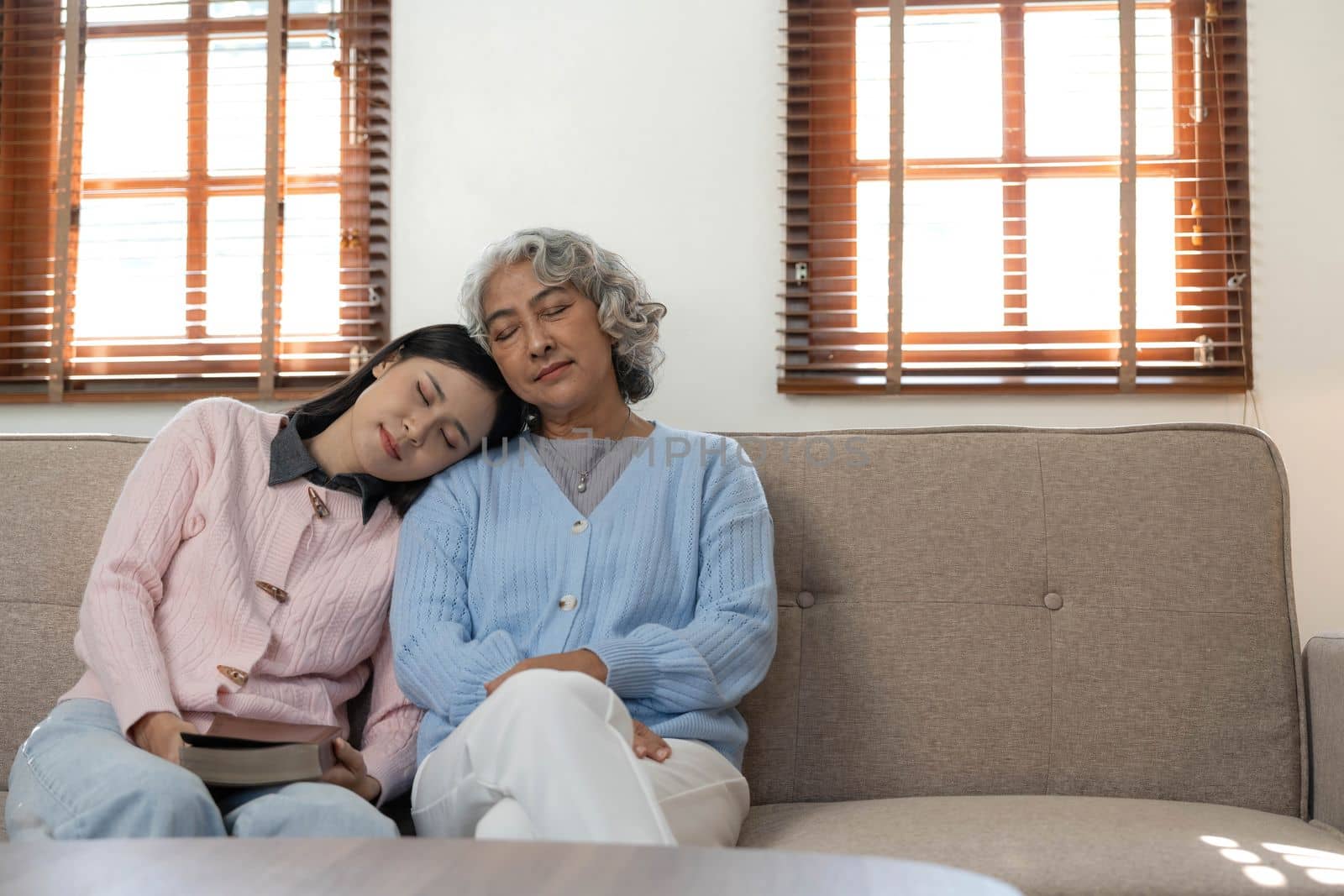 Woman reading a book while sitting with happy grandmother at home by wichayada