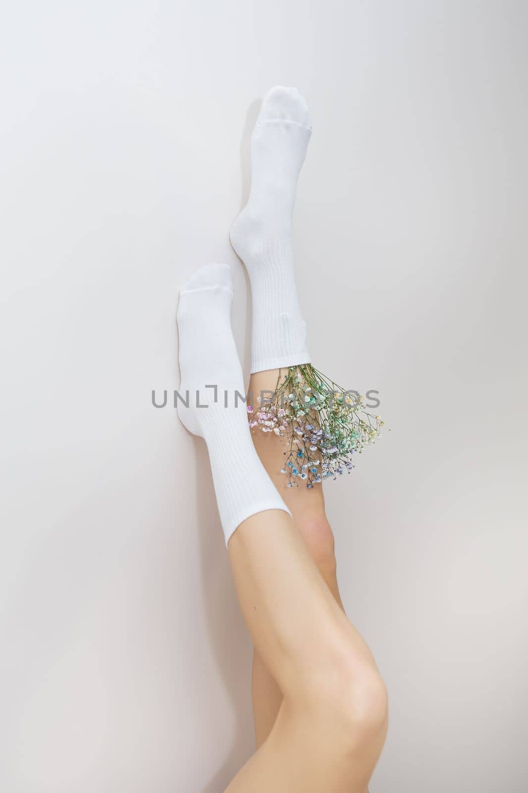 The legs of a girl in white socks in which there are flowers stand up. The concept of smooth and beautiful legs