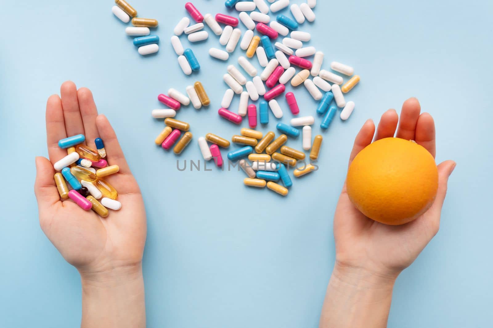 Many multi-colored pills, man's hands in one vitamins in another fresh orange. Health and treatment alternatives concept