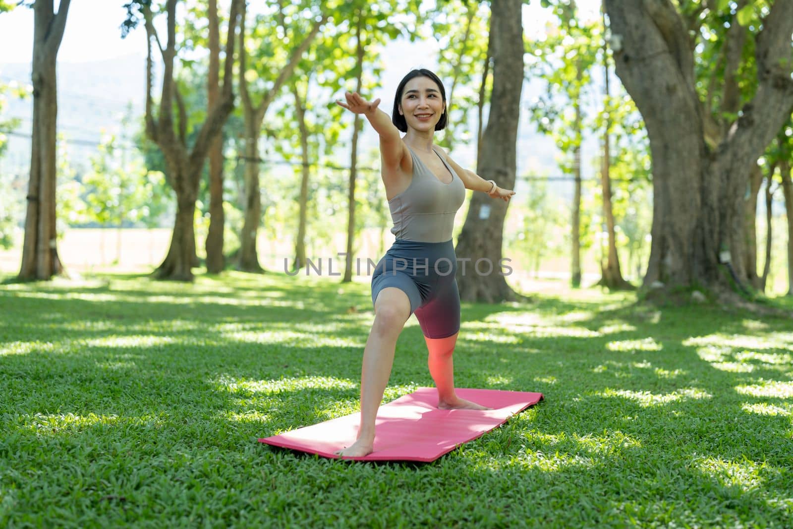 Young attractive girl is doing advanced yoga asana on the fitness mat in the middle of a park