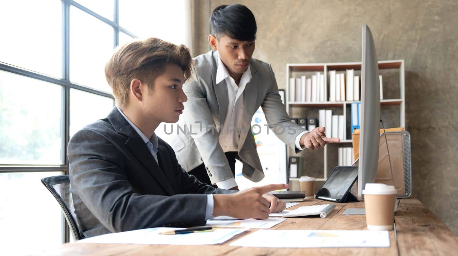 Two young Asian businessman talk, consult, discuss working with new startup project idea presentation analyze plan marketing and investment in the office...