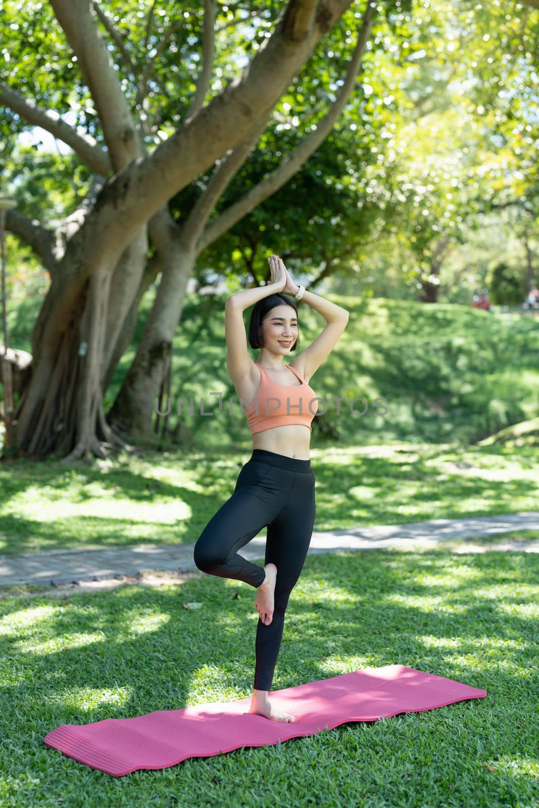 Young attractive girl is doing advanced yoga asana on the fitness mat in the middle of a park. by nateemee