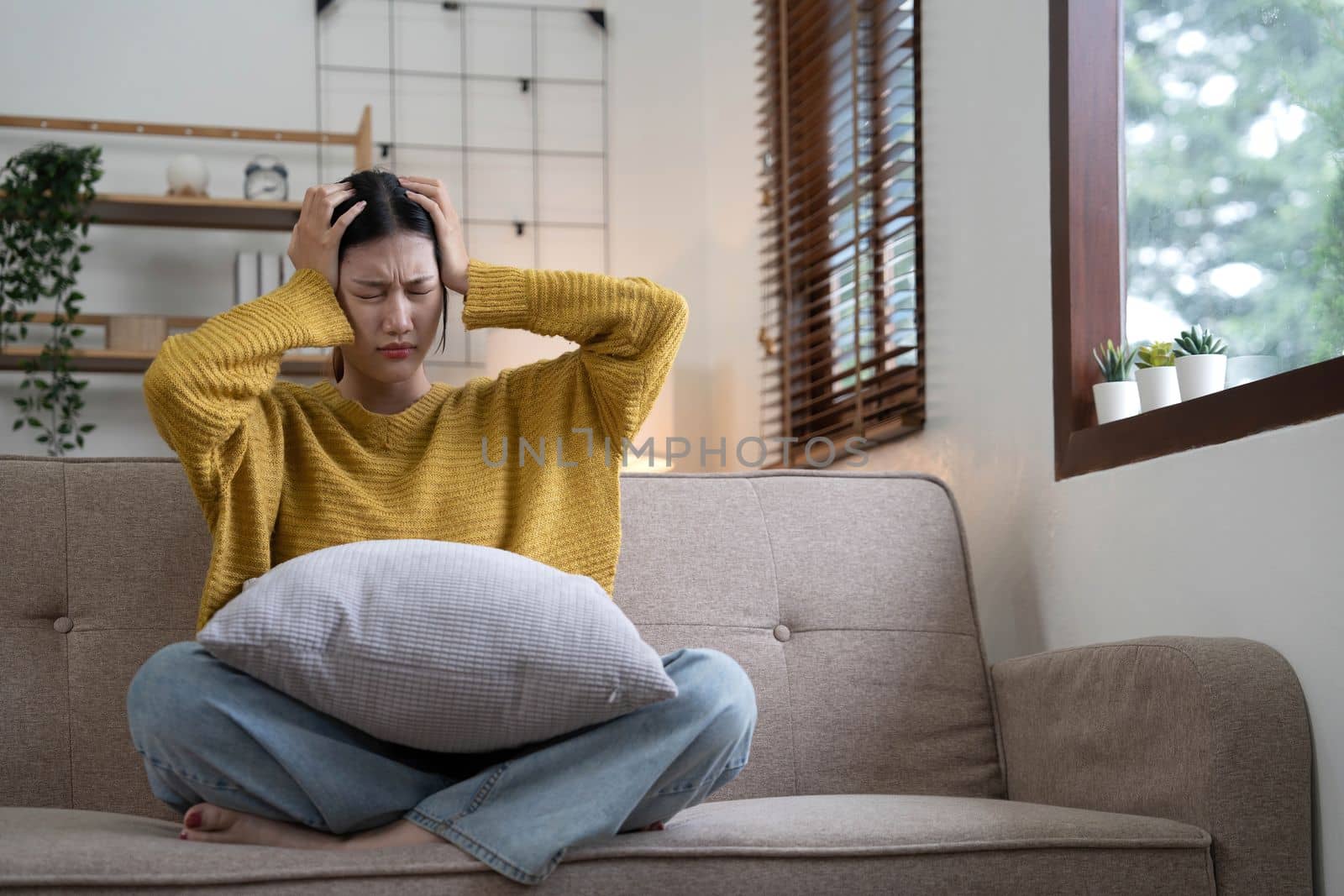 Hand on temples of young unhappy sadness Asian girl sitting on sofa. She is feeling not very good due to her sickness and having a headache. Seen from the front. Stress and sickness concept...