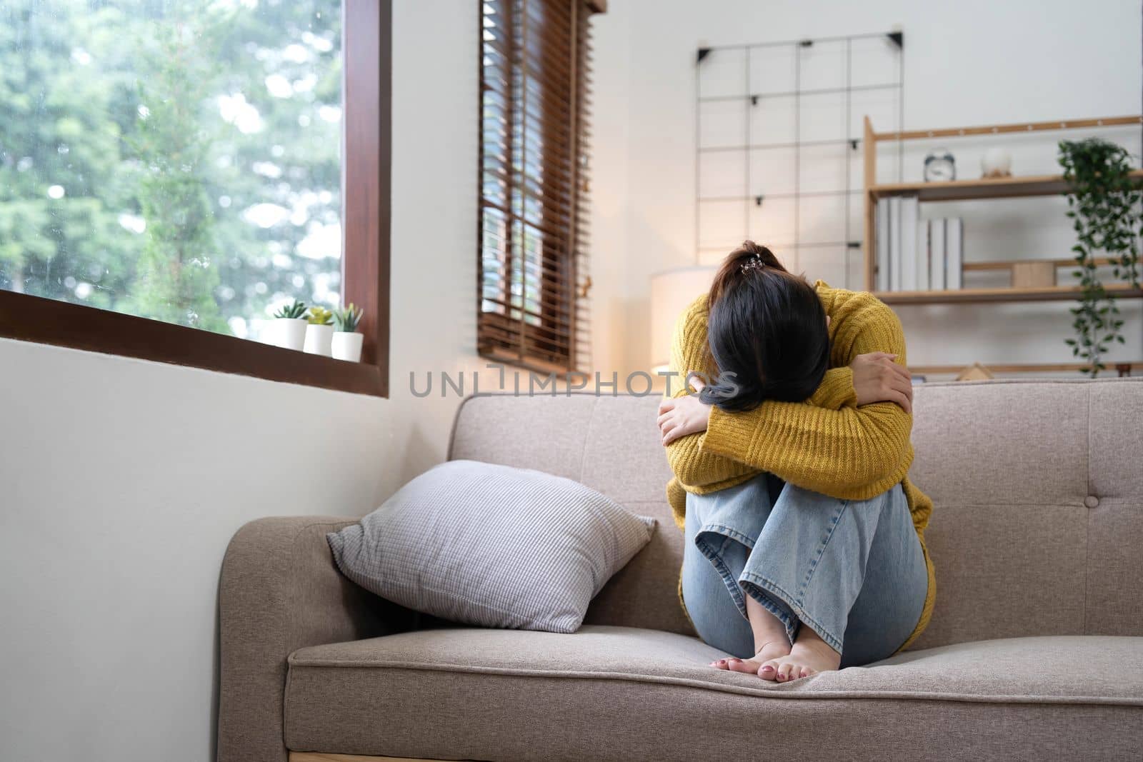 Hand on temples of young unhappy sadness Asian girl sitting on sofa. She is feeling not very good due to her sickness and having a headache. Seen from the front. Stress and sickness concept..