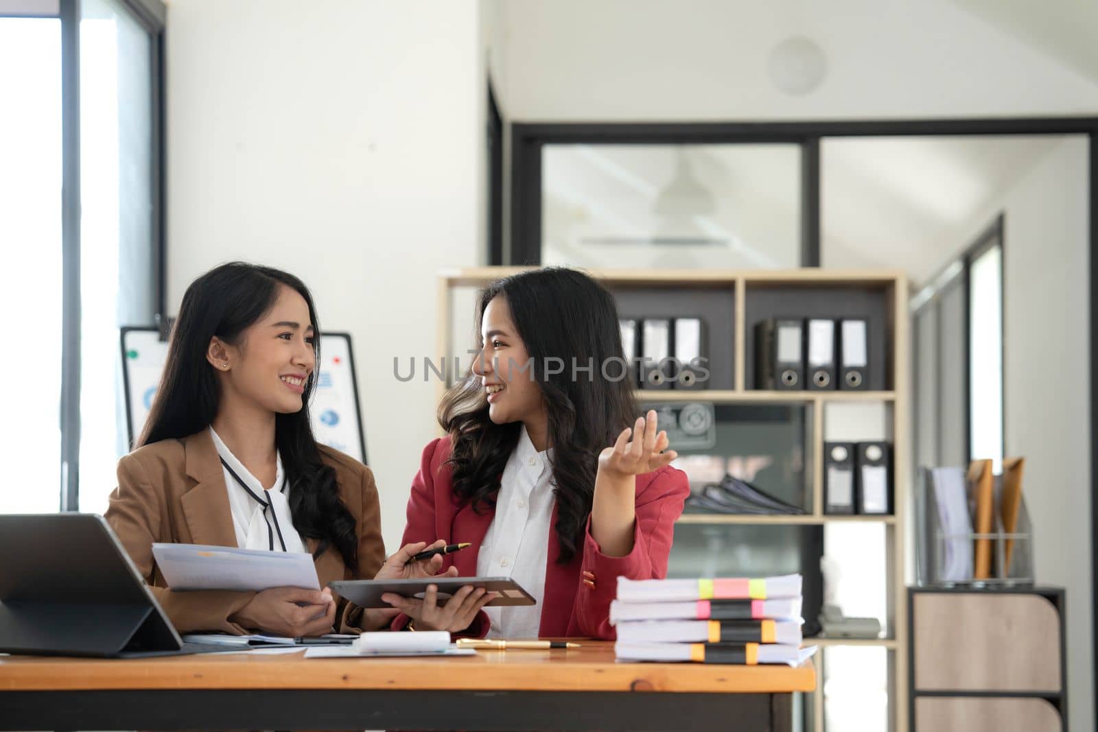 Two young Asian business woman talk, consult, discuss working with new startup project idea presentation analyze plan marketing and investment in the office. by wichayada