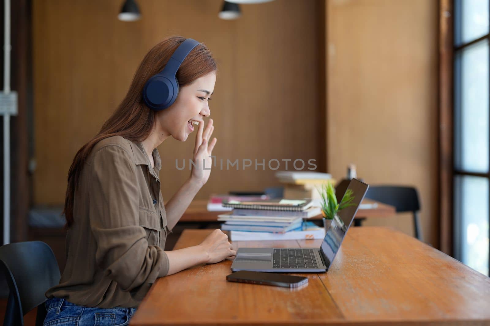 Asian tutor of language start online lesson with trainee wave hand smiling looks at pc screen. woman in headphones communicating distantly, e-learning process, application usage concept.