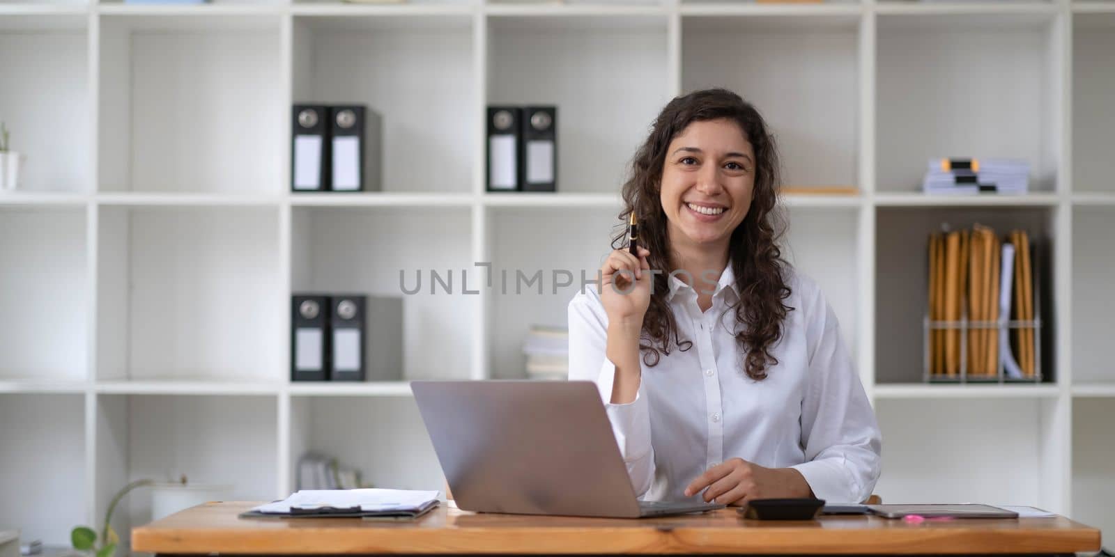 Photo of cheerful young woman working using computer laptop concentrated and smiling at office..