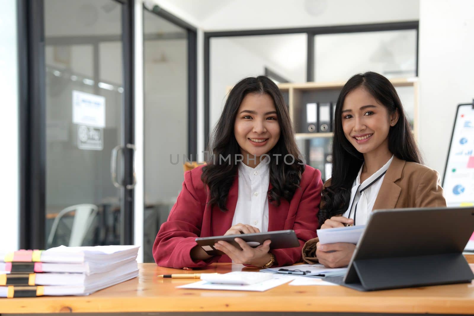 Two young Asian business woman talk, consult, discuss working with new startup project idea presentation analyze plan marketing and investment in the office..