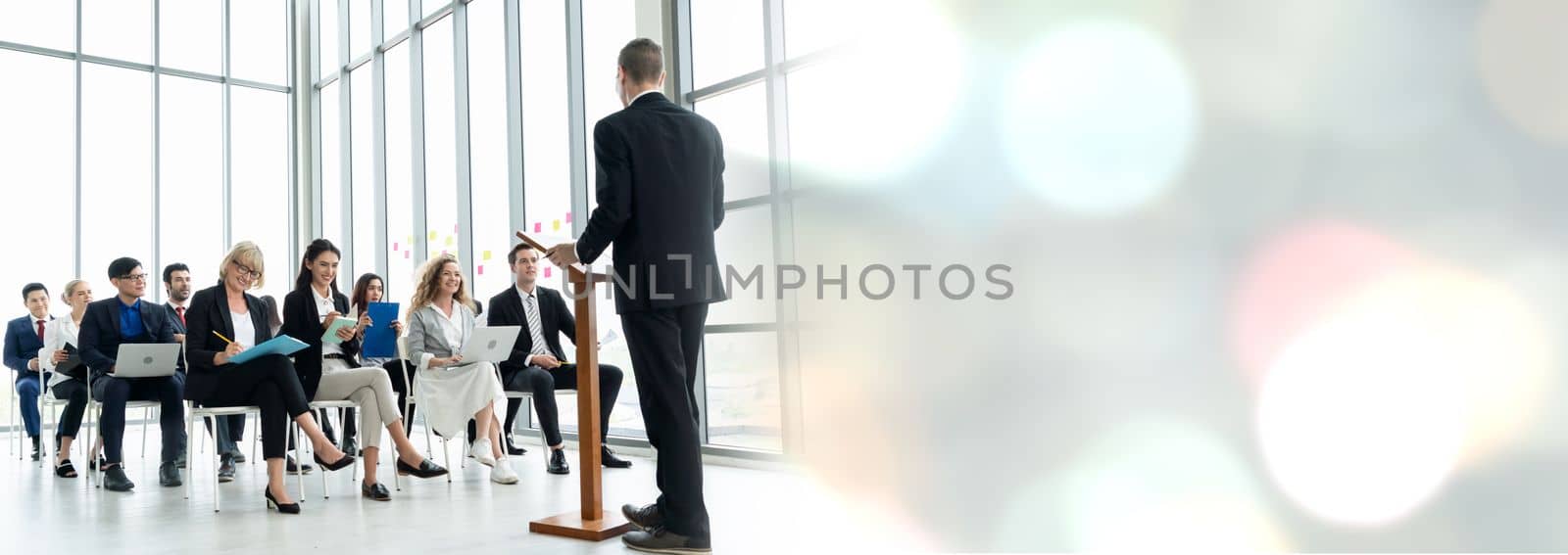 Group of business people meeting in a seminar conference widen view . Audience listening to instructor in employee education training session . Office worker community summit forum with speaker .