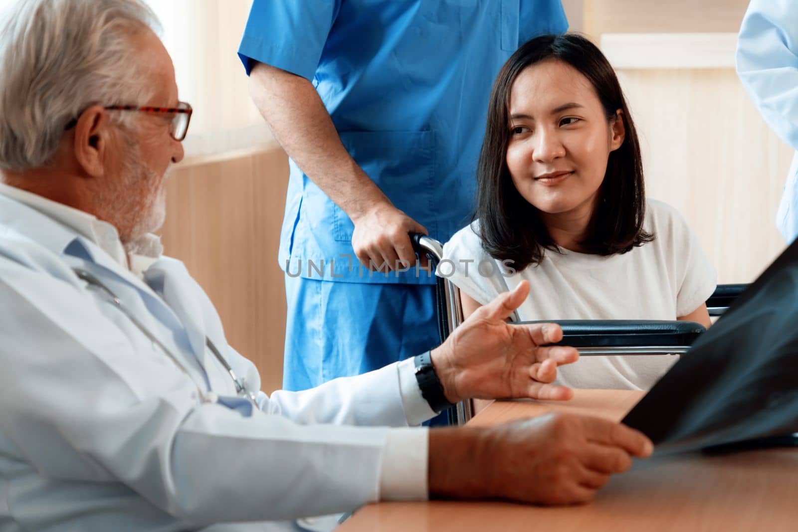 A young adult patient in a wheelchair accompanied by male nurse discusses her health problem with her doctor in sterile room. Doctor consult his patient about her symptom with radiograph.