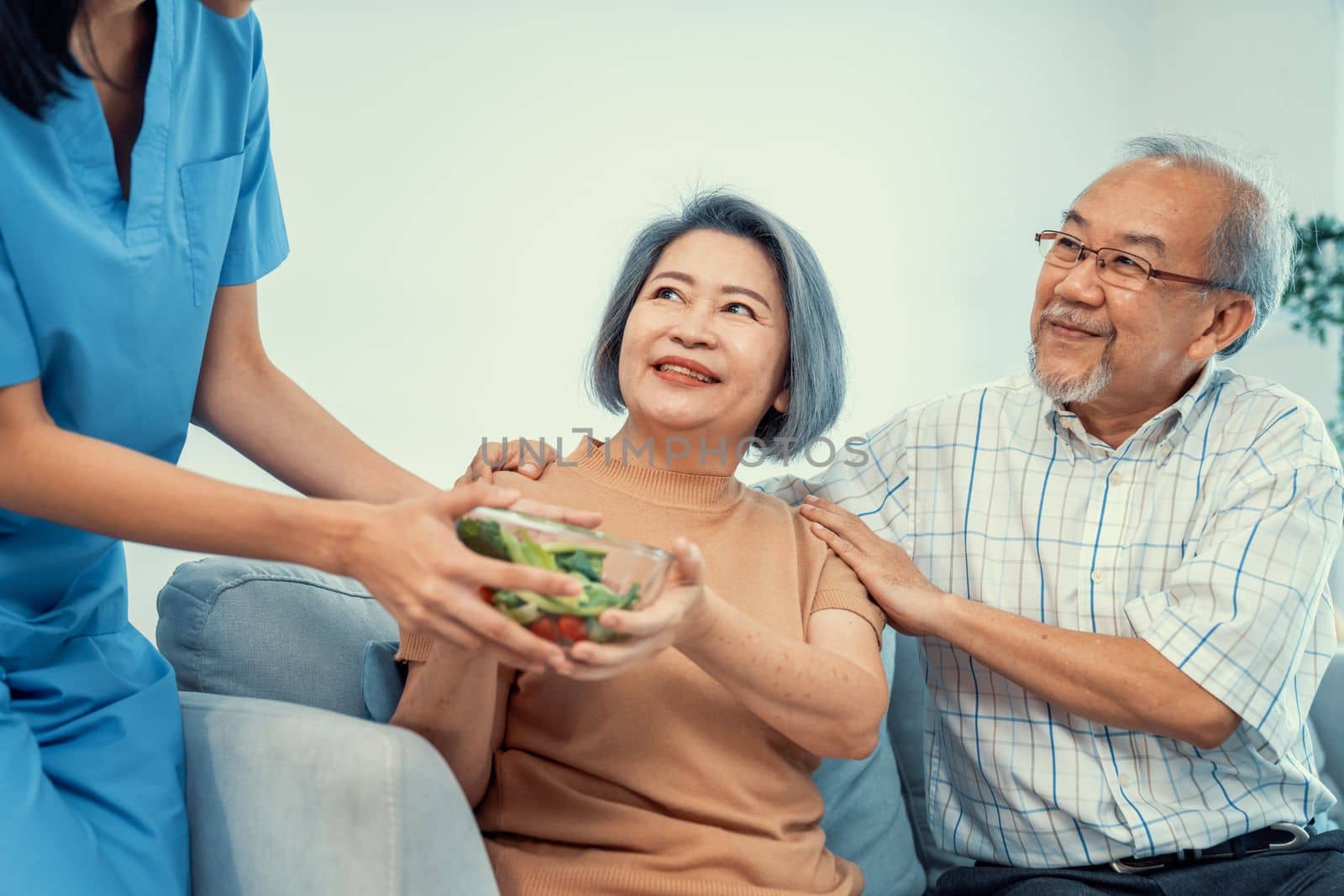 A female nurse serves a bowl of salad to a contented senior couple. Health care and medical assistance for the elderly, nursing home for pensioners.