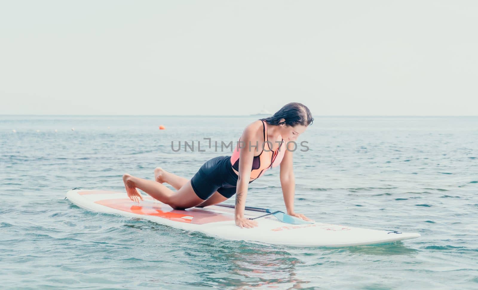 Woman sup yoga. Happy young sporty woman practising yoga pilates on paddle sup surfboard. Female stretching doing workout on sea water. Modern individual female outdoor summer sport activity