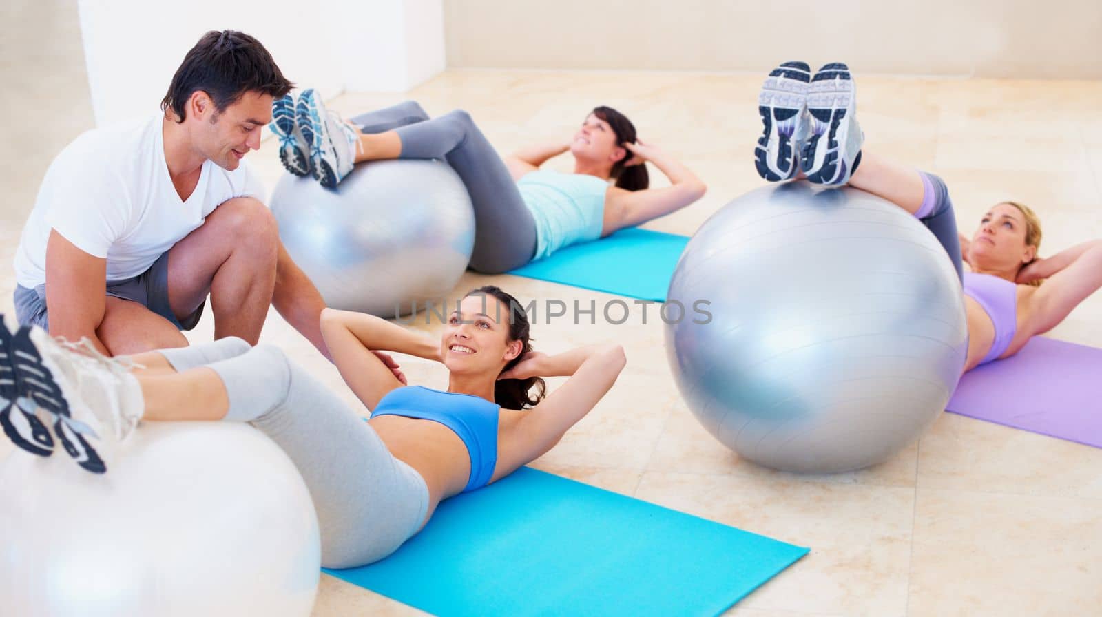 Getting skilled fitness advice. Young woman doing a sit up during a pilates class with the help of an instructor. by YuriArcurs