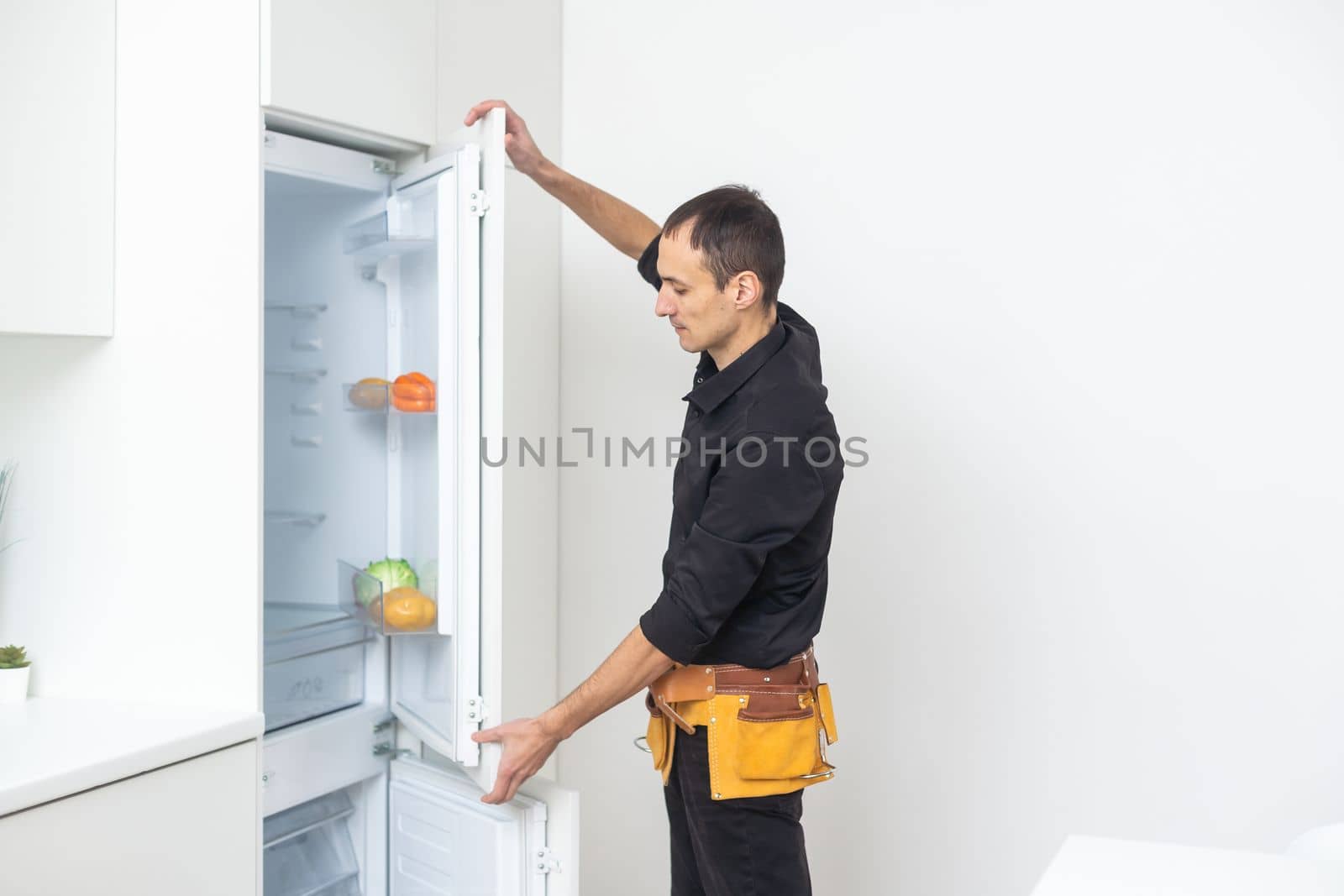 Young Male Repairman Fixing Refrigerator In Kitchen.