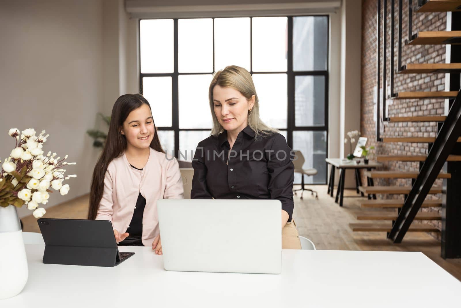 Mother is working with laptop when her daughter is using digital tablet