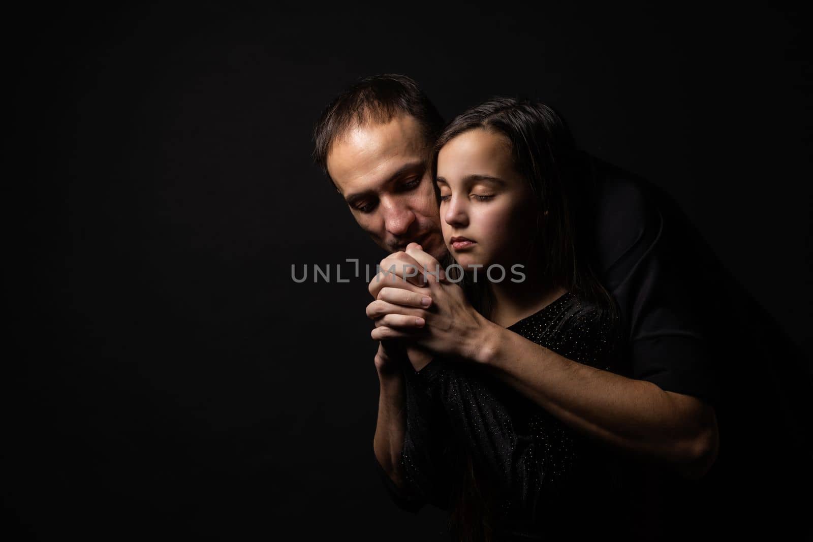 Young father and daughter praying with hands together with hope expression on face very emotional and worried