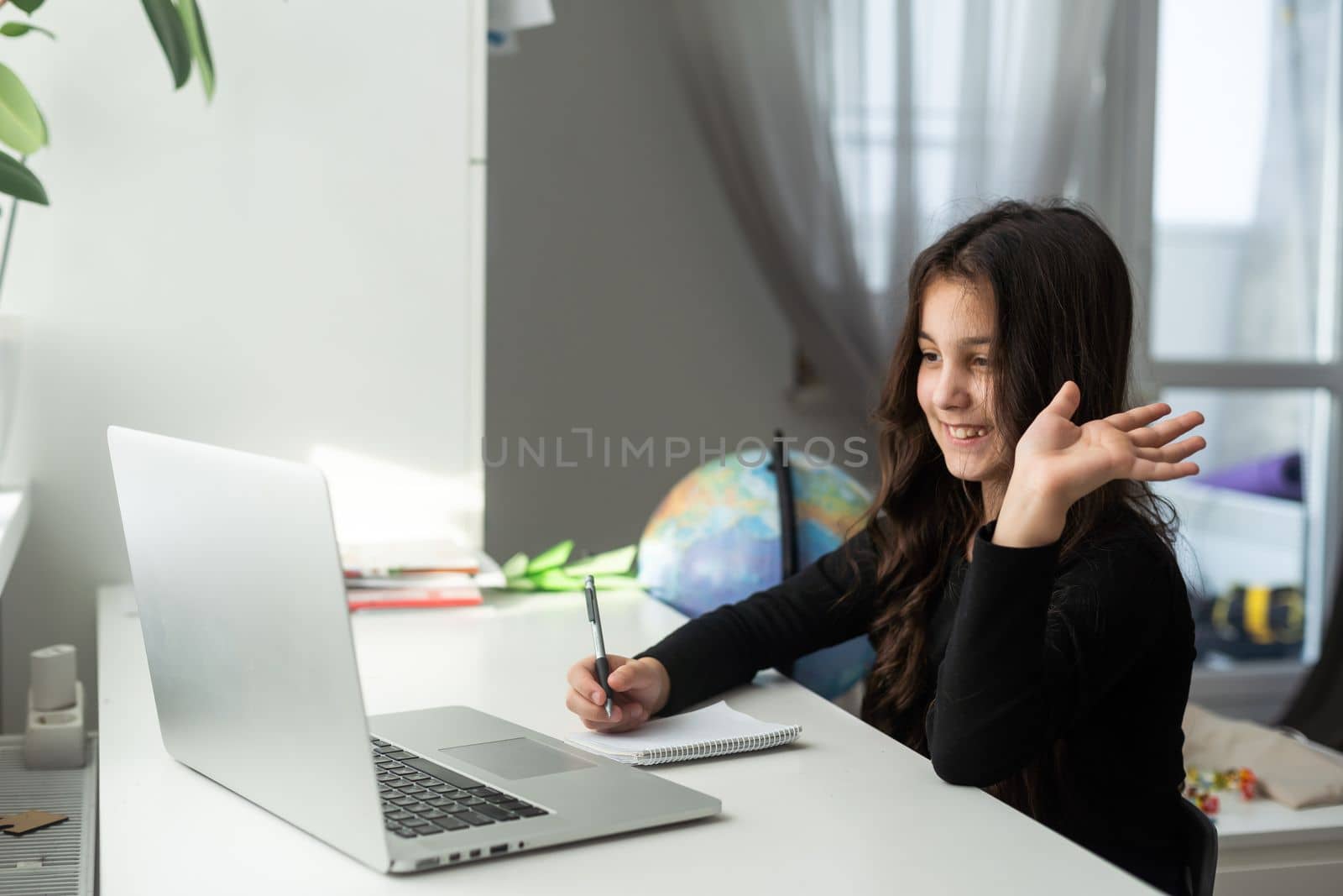 Home schooling. A girl is sitting at a table with a laptop during an online video chat of a school lesson with a teacher and class. Concept of distance education. Self-isolation in quarantine