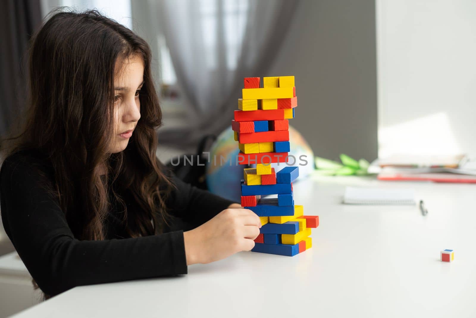 a little happy girl is playing the board game jenga at the table. Construction of a tower made of wooden cubes.