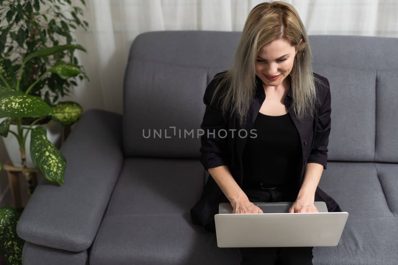 Smiling young woman using laptop, sitting on couch at home, beautiful girl shopping or chatting online in social network, having fun, watching movie, freelancer working on computer project
