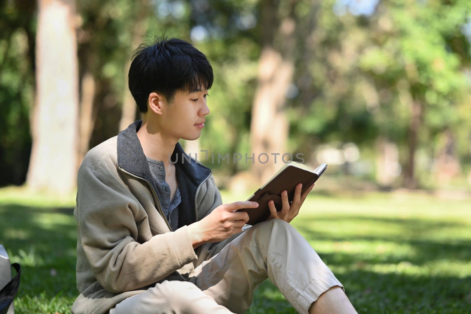 Peaceful college student reading book, relaxing on campus lawn. Education and lifestyle concept.