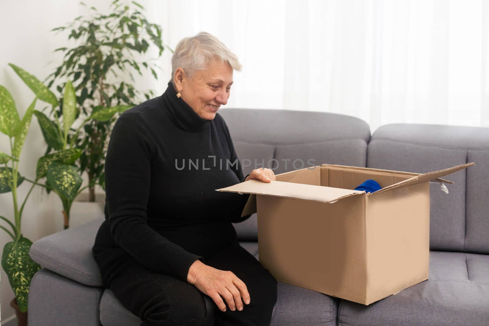 Elderly woman unpacking things in new house. Female hands opening cardboard box. Real estate, purchase, moving concept