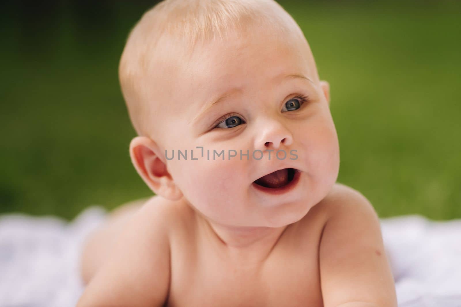 Cute happy toddler lying on a blanket on the grass outdoors in summer.