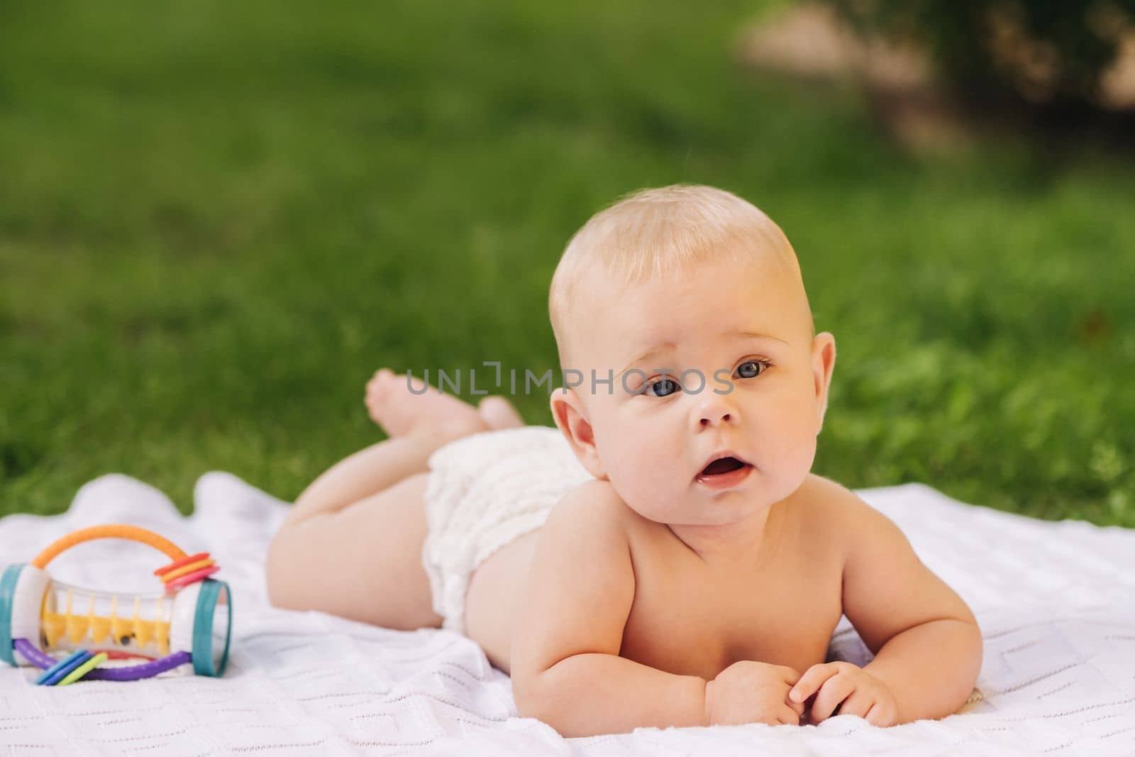 Cute happy toddler lying on a blanket on the grass outdoors in summer.