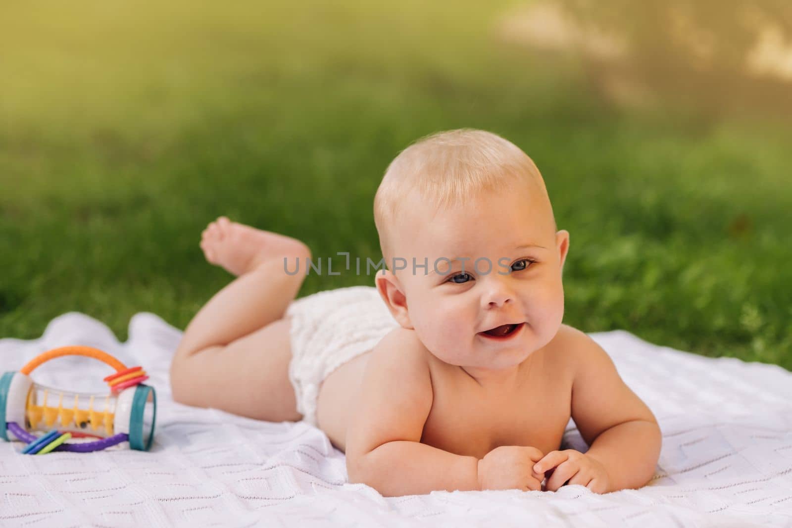 Cute happy toddler lying on a blanket on the grass outdoors in summer.