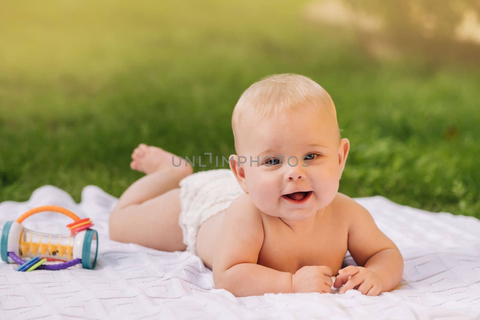 Cute happy toddler lying on a blanket on the grass outdoors in summer.