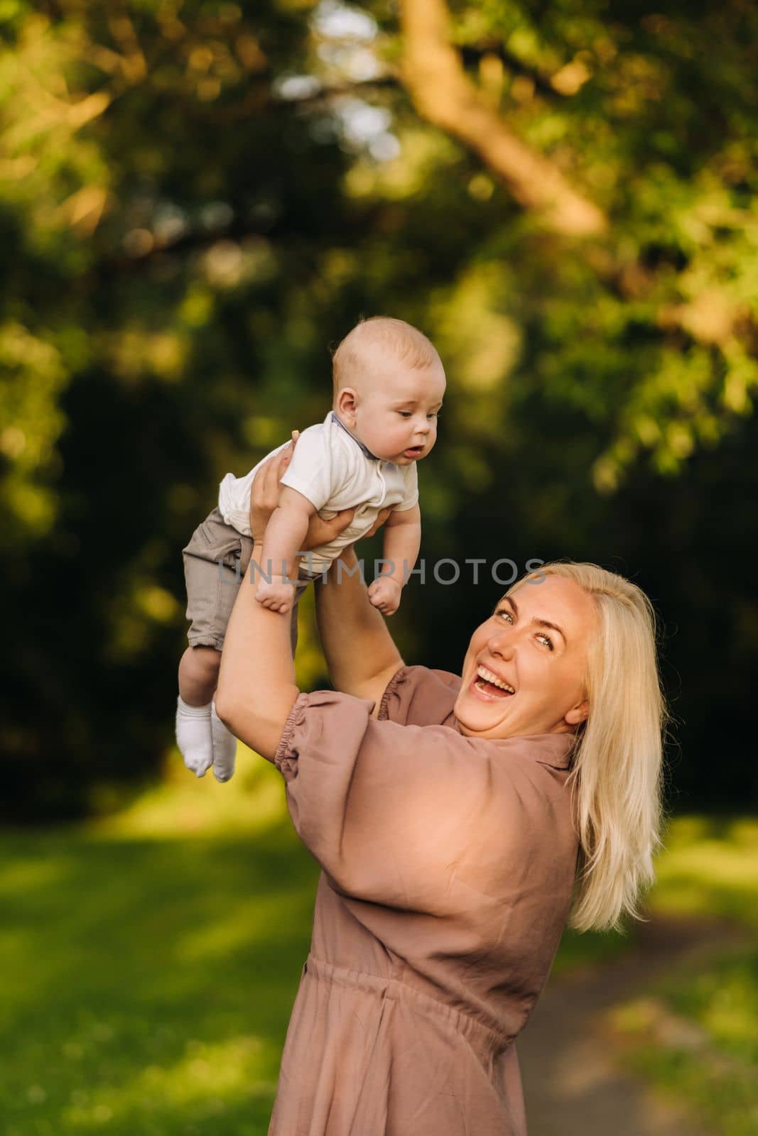 A mother holds a happy baby boy in her arms in a summer park.