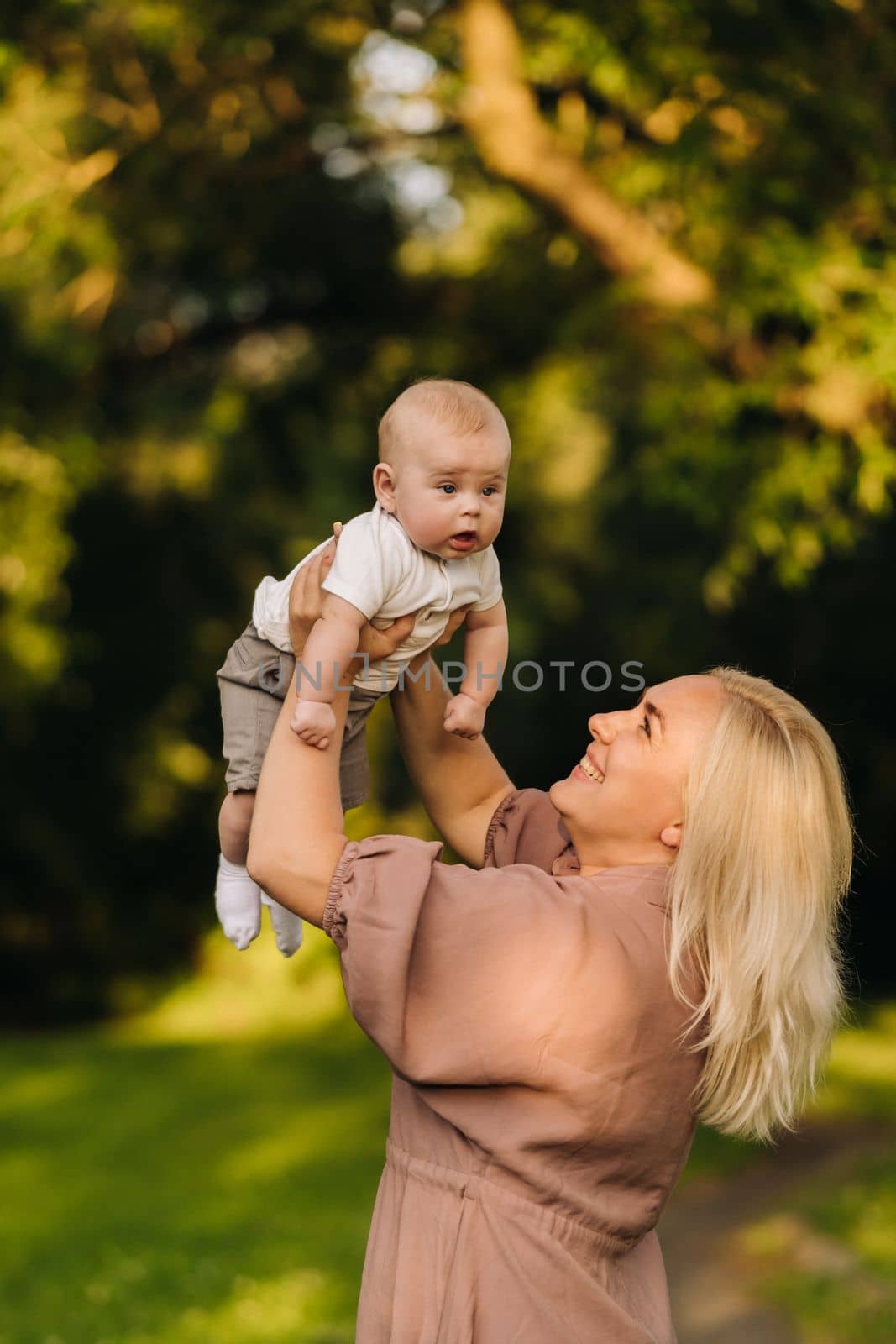 A mother holds a happy baby boy in her arms in a summer park by Lobachad