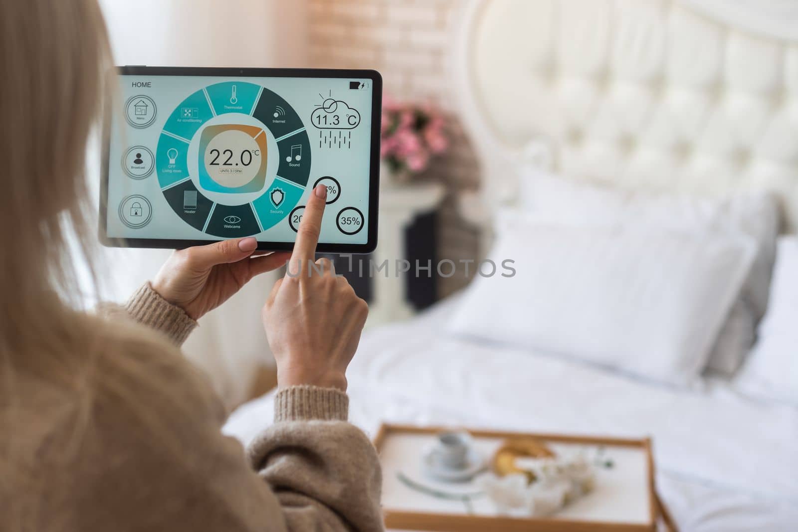 Woman controlling smart home devices using a digital tablet with launched application in the white living room. Smart home concept.