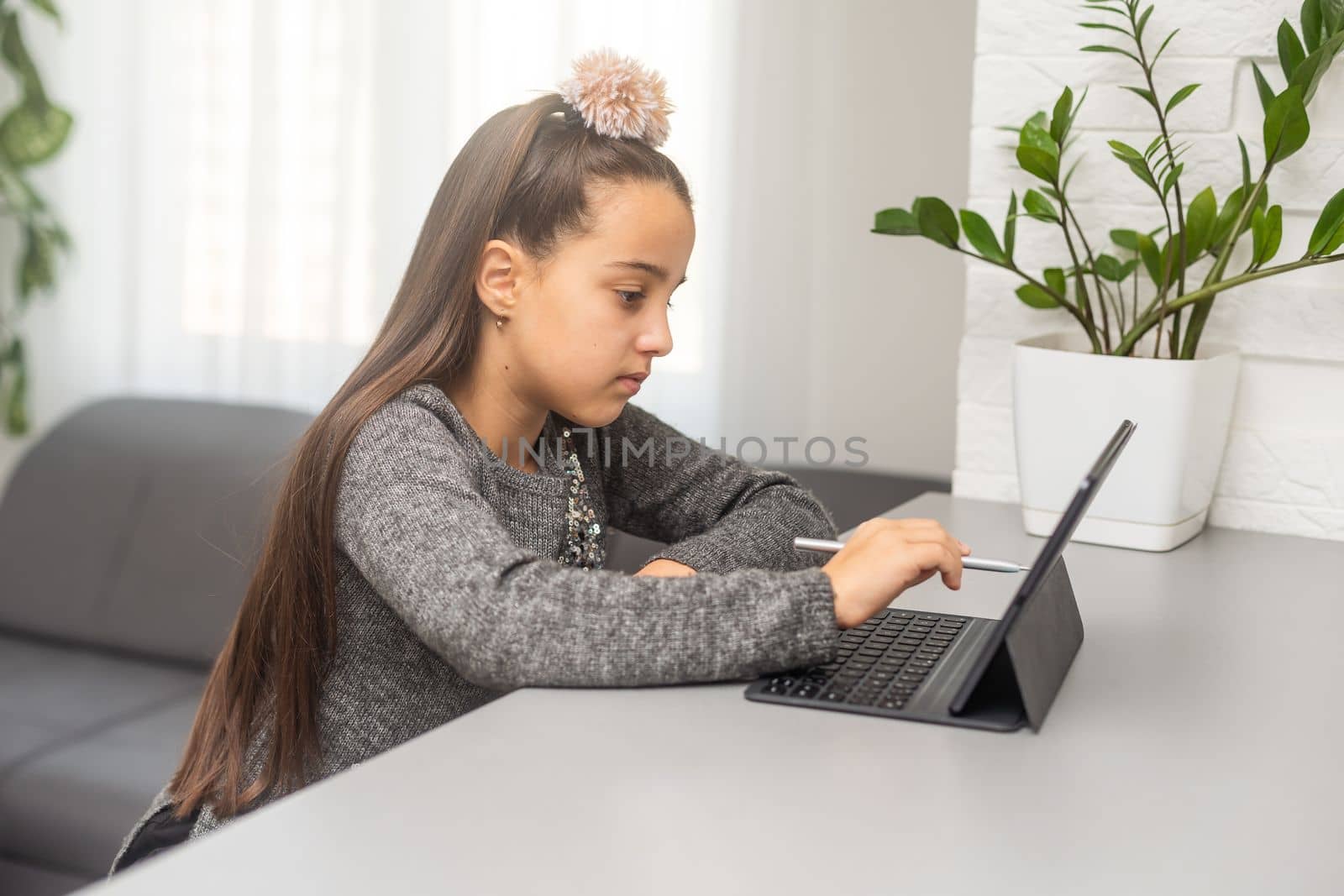 school kid girl student using digital tablet looking at screen at desk. Online education, virtual classes software tech ads by Andelov13