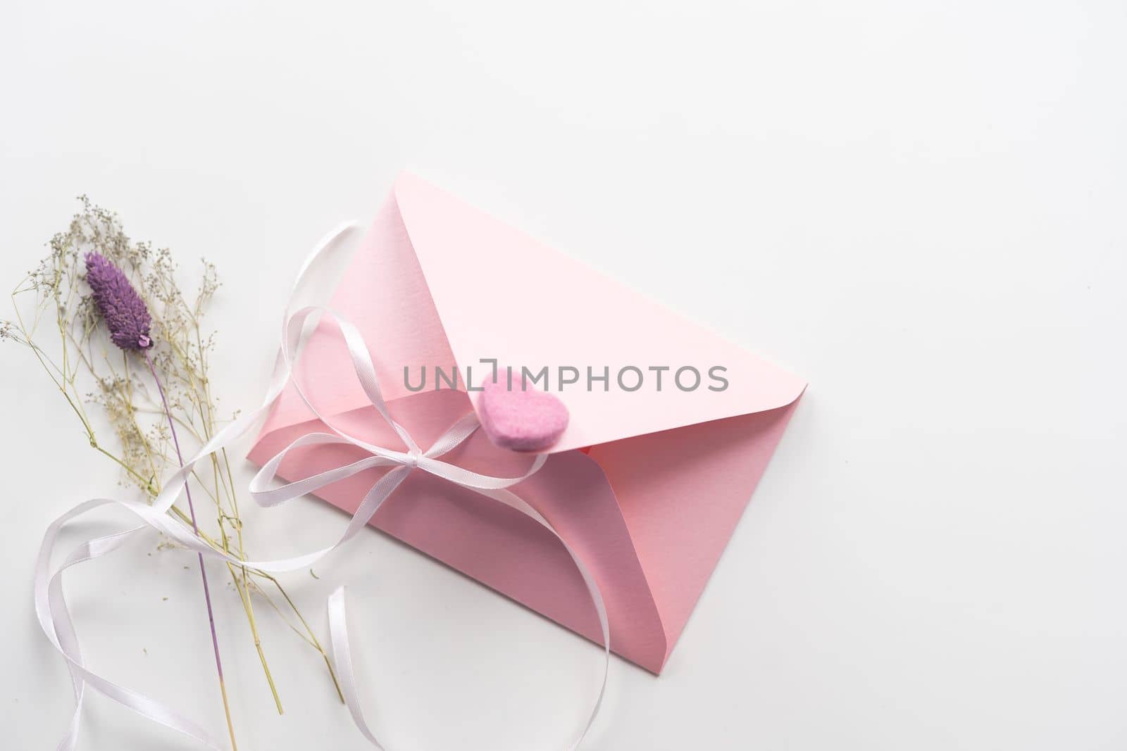 Minimal composition with a pink envelope, white blank card and a wax flower on a white background. Mockup with envelope and blank card. Flat lay. Top view