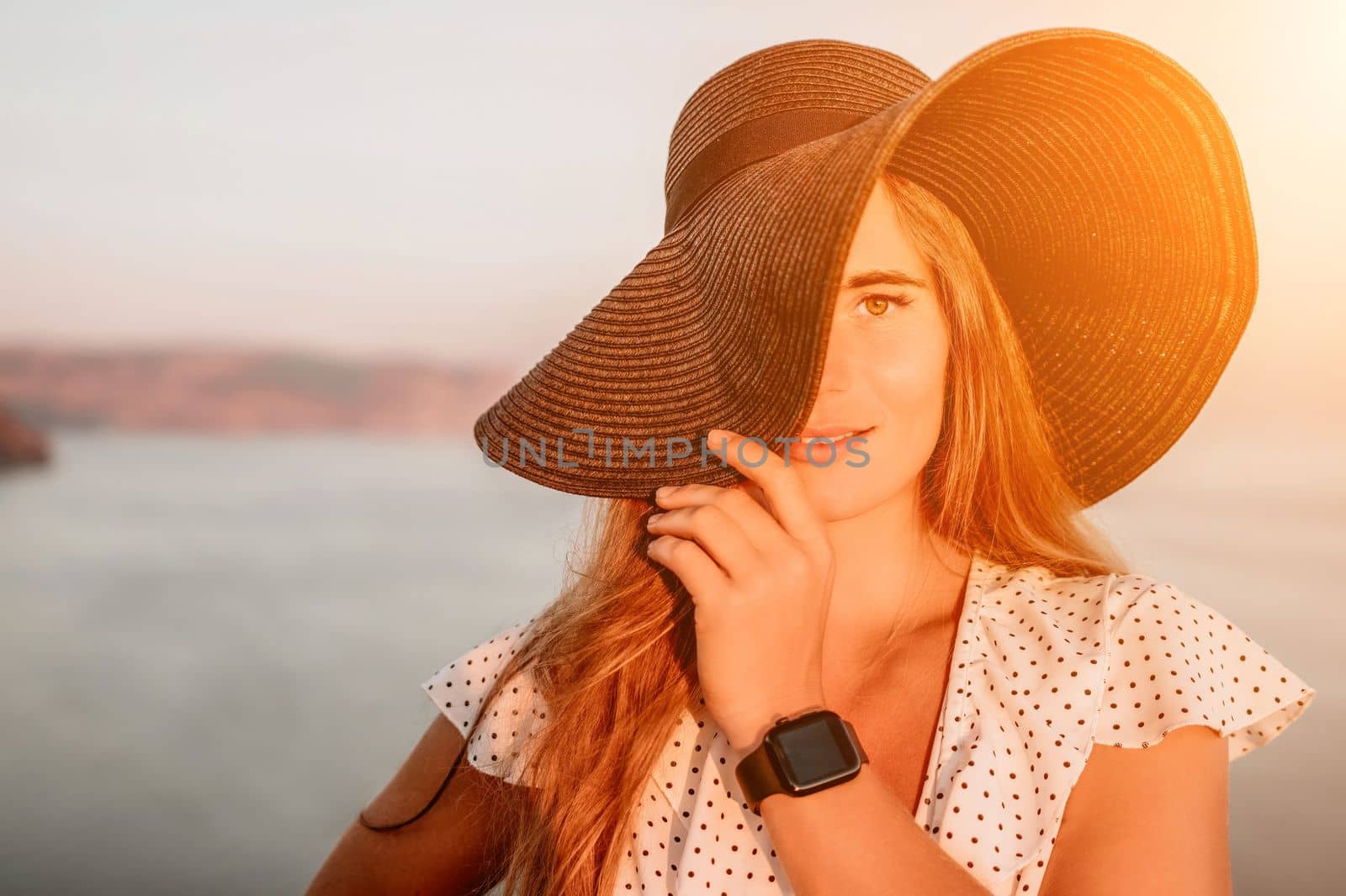 Portrait of happy young woman wearing summer black hat with large brim at beach on sunset. Closeup face of attractive girl with black straw hat. Happy young woman smiling and looking at camera at sea