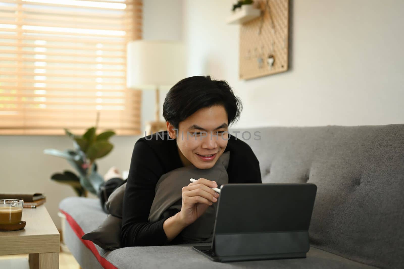 Smiling Asian man using computer tablet on sofa at home.