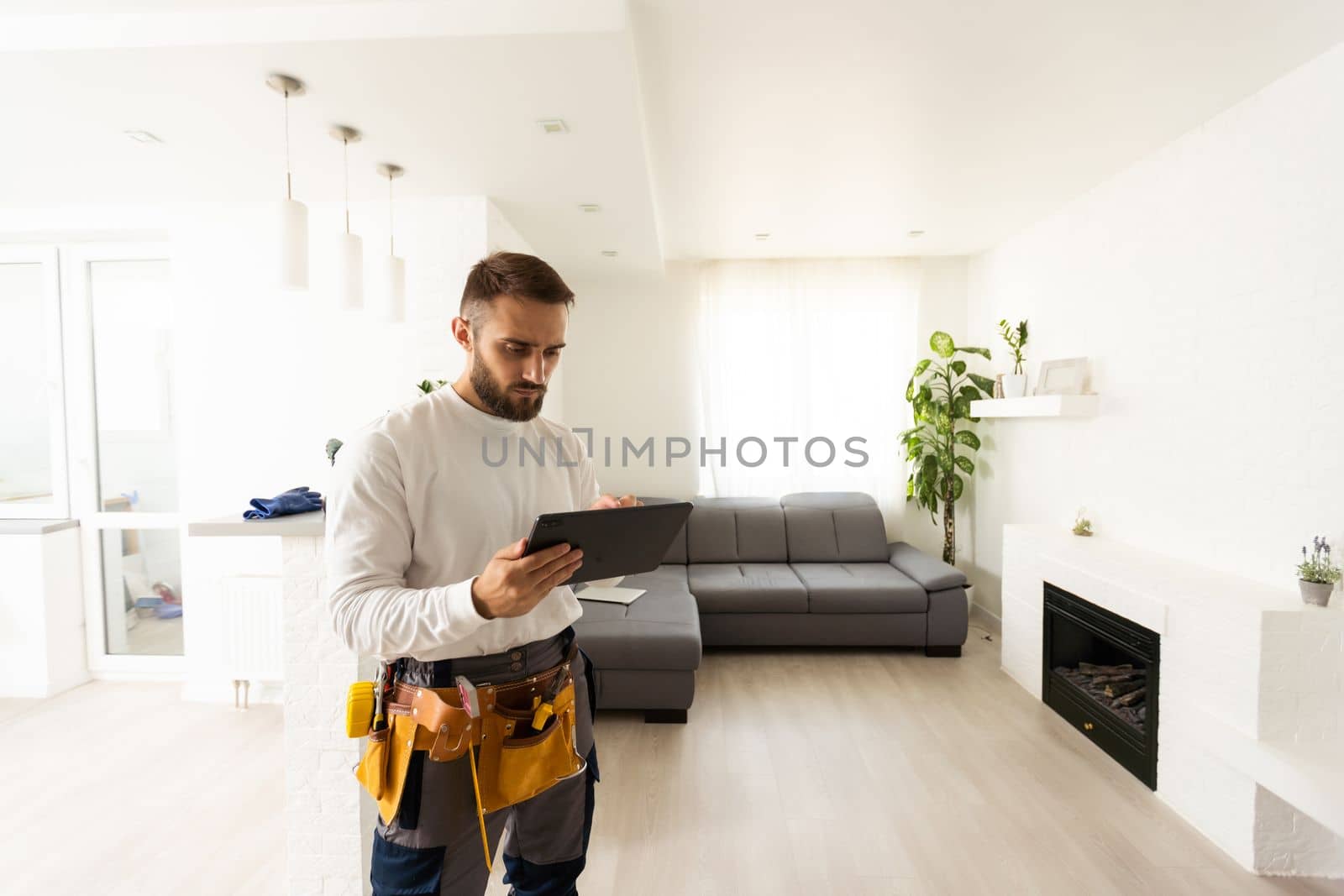 repair, construction and building concept - happy smiling worker or builder with tablet pc computer and tools over home room background