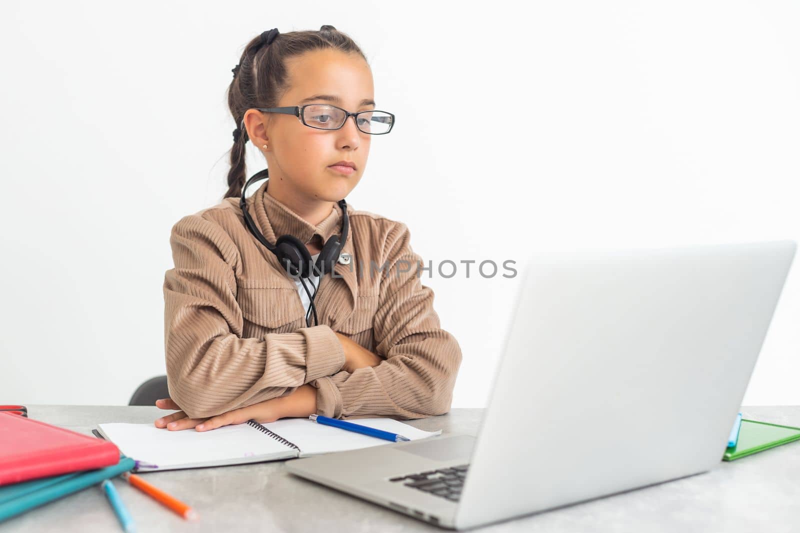 Portrait of little girl in wireless headset using laptop, studying online at home, interested happy student typing on keyboard looking at pc screen, watching webinar, online course, doing homework. by Andelov13