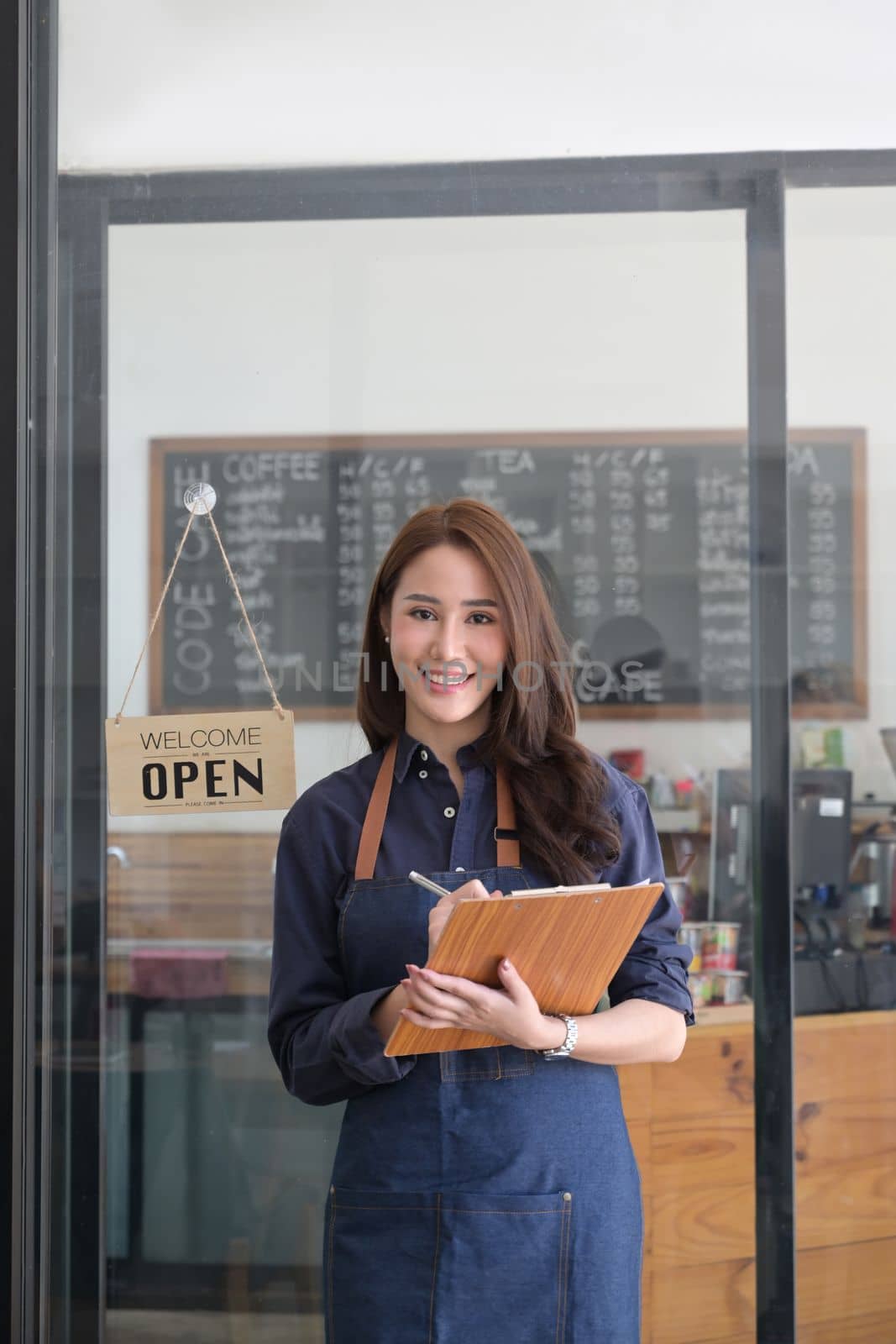 Female entrepreneur holding clipboard of menu and standing in coffee shop. by prathanchorruangsak