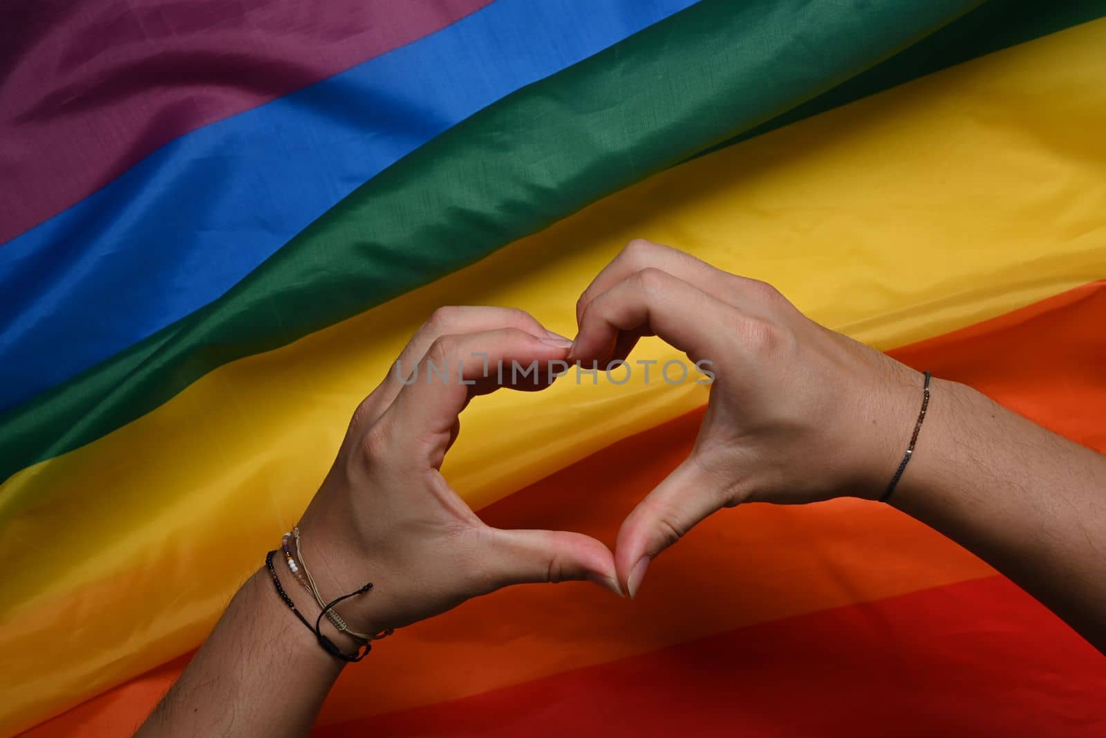 Hand making a heart sign over LGBT rainbow flag.