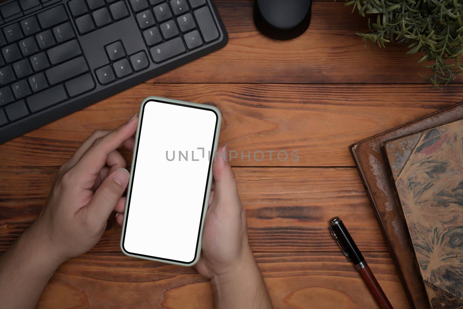 Man holding mock up smart phone with white screen over wooden table.