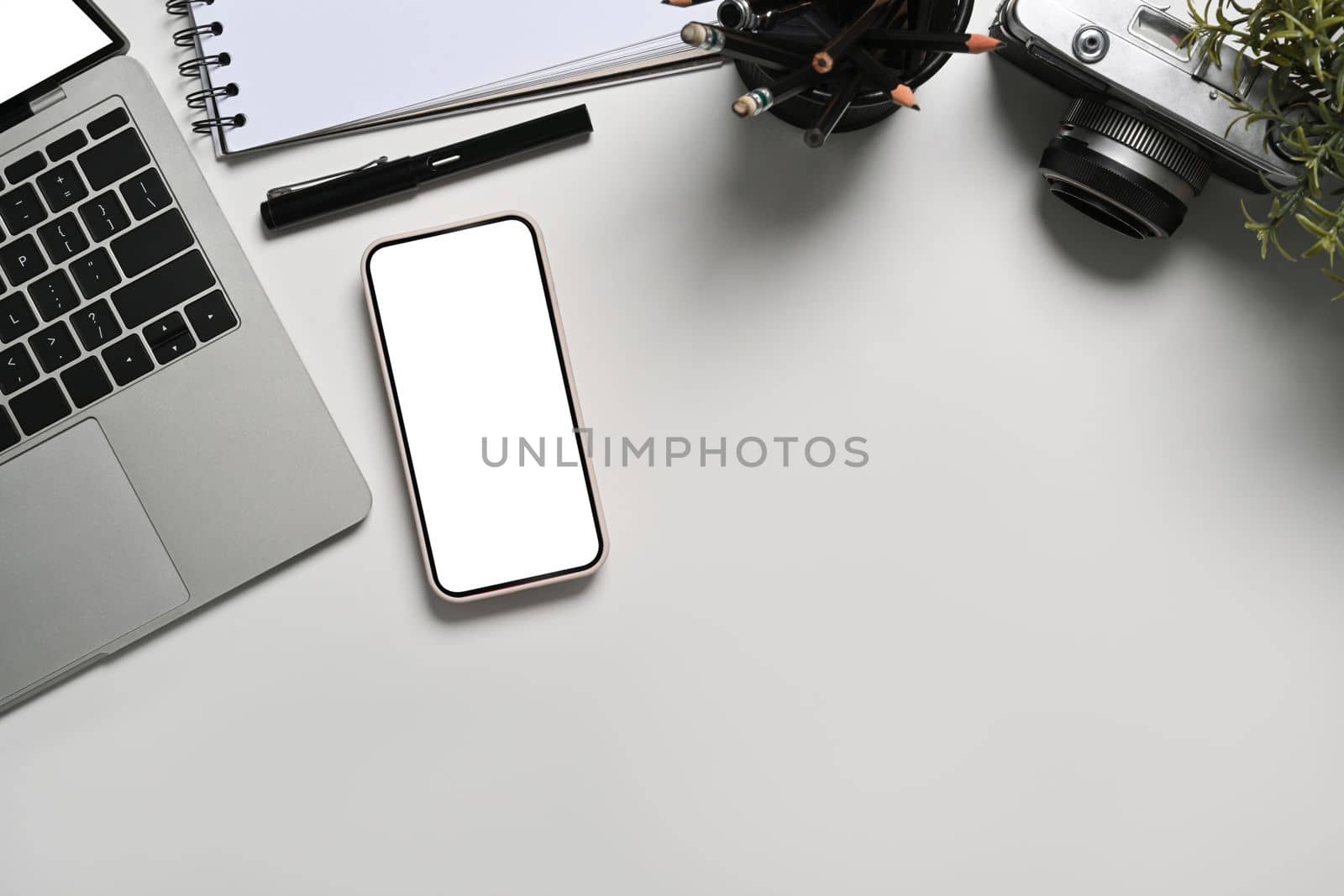 Mock up mart phone with empty screen, laptop, notebook and camera on white table. by prathanchorruangsak