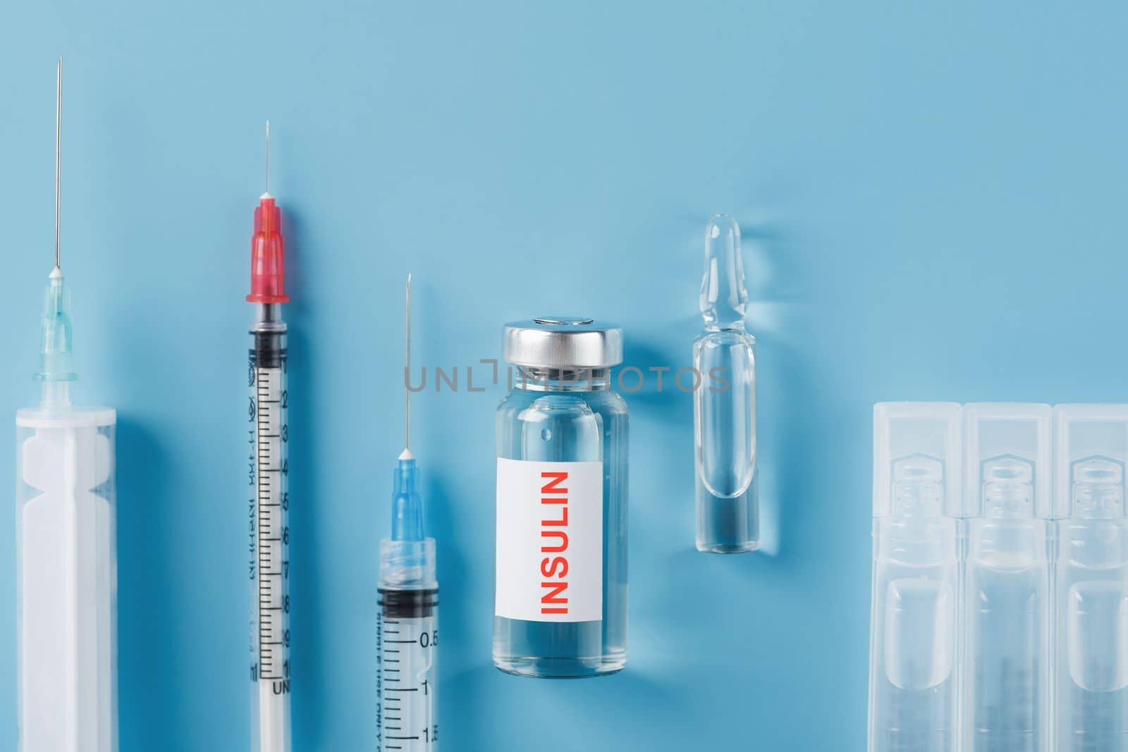 Medicine in ampoules with insulin, needles and syringes for medical subcutaneous injection on a blue background