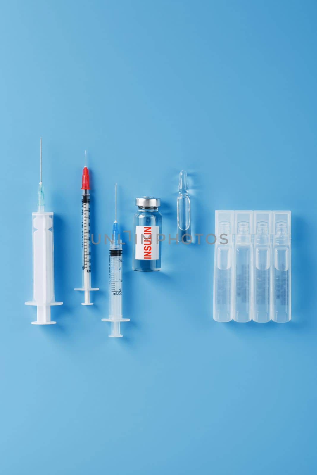 Ampoule bottle with insulin, needles and syringes for medical subcutaneous injection on a blue background